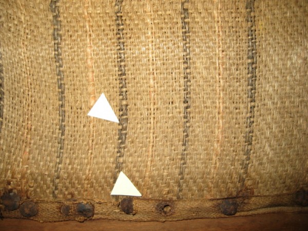 Detail of the camp bed sacking, showing the faded black and red stripes. The paper arrows indicate areas where fiber samples were collected. 