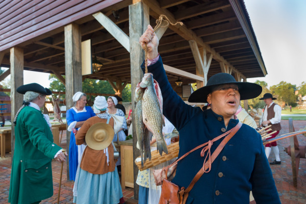 Interpreter Kody Grant offers fish for sale at 18th century Market House scene