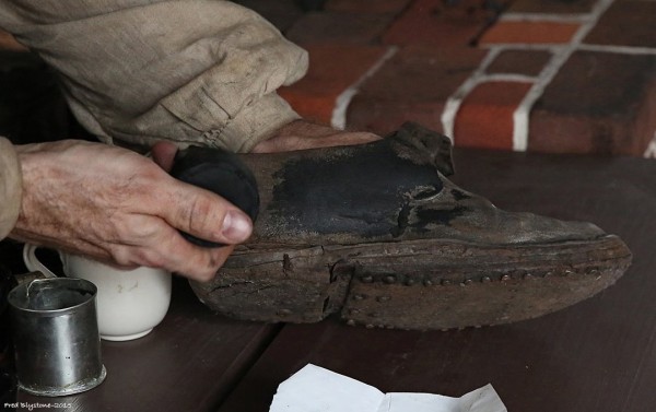 Shoemaker Rob Welch applies black ball to a leather shoe.